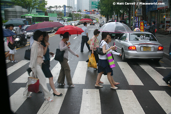 people crossing street with umbrellas