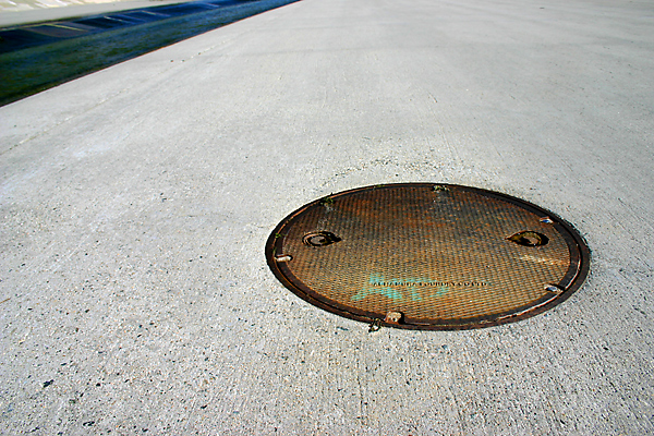 manhole on pavement with flowing river in background